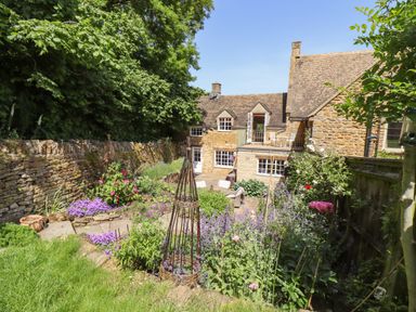A garden with flowers and plants in front of a stone house at 1 The Lane in Chipping Norton