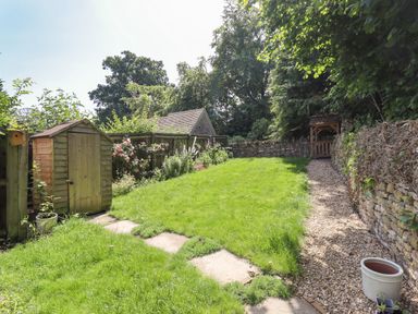 A garden with a wooden shed a grass lawn flowers along a fence and a gravel path with a wooden gate at 1 The Lane in Chipping Norton