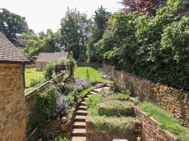 A garden with stone steps and flower beds next to a stone wall and wooden fence at 1 The Lane in Chipping Norton