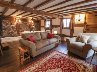 A living room with two grey sofas a red patterned rug wooden beams and a dining table with flowers at 18 Church Street in Llangollen