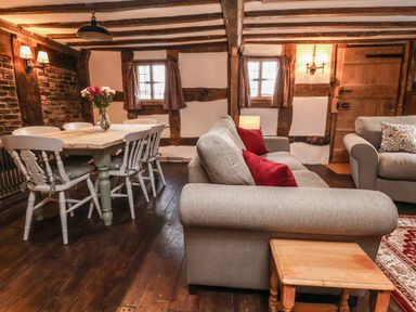 A living room with a dining table and chairs sofa with red cushions and a wooden side table at 18 Church Street in Llangollen