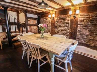 A dining room with a wooden table and chairs a vase with flowers on the table and a spiral staircase in a rustic room at 18 Church Street in Llangollen