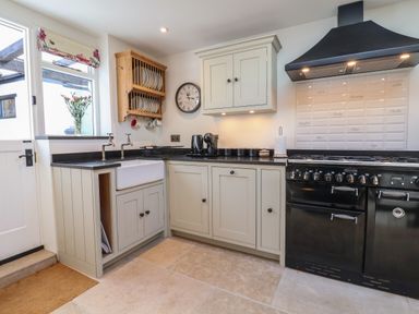 A kitchen with a sink two taps and cupboards a clock a stove with an extractor fan and utensils at 18 Church Street Llangollen