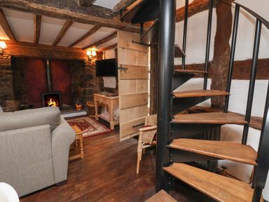 A living room with a spiral staircase a gray sofa a wooden coffee table a fireplace and a wall mounted television at 18 Church Street in Llangollen