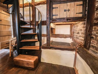 An interior space with a wooden spiral staircase wicker chair and exposed brick and wooden beams at 18 Church Street in Llangollen
