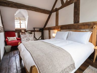A bedroom with a large bed white bedding wooden beams a red armchair and a chest of drawers at 18 Church Street Llangollen