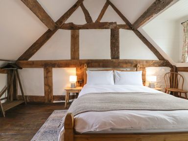 A bedroom with a wooden bed frame two nightstands with lamps a wooden chair a small rug and exposed wooden beams at 18 Church Street in Llangollen