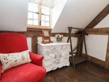 A corner of a room with a red armchair a white distressed dresser with a mirror and flowers and a wooden clothes rack at 18 Church Street in Llangollen