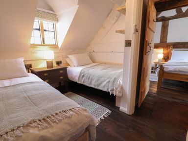 A bedroom with two single beds a bedside table with a lamp and a window showing another room with a double bed and a lamp at 18 Church Street in Llangollen