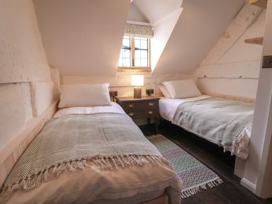 A bedroom with two single beds and a nightstand with a lamp under a window at 18 Church Street in Llangollen