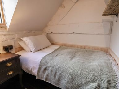 A single bed with pillows and a blanket beside a wooden nightstand under a slanted ceiling at 18 Church Street in Llangollen