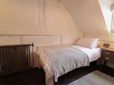 A single bed with a pillow and blanket next to a radiator and bedside table in a small room at 18 Church Street in Llangollen