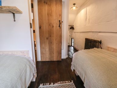 A small bedroom with two beds covered by beige patterned blankets a wooden door and a radiator at 18 Church Street in Llangollen