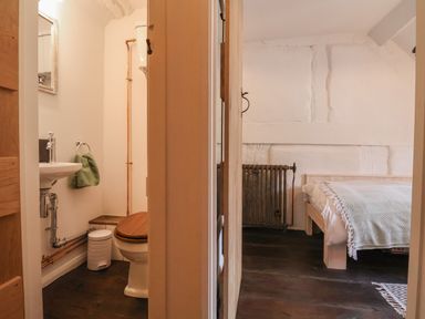 A small bathroom with a toilet and sink next to a bedroom with a bed and radiator at 18 Church Street in Llangollen
