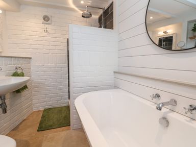 A bathroom with a white bathtub sink a green towel green bath mat and a shower with a rain showerhead at 18 Church Street in Llangollen