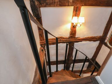 A wooden spiral staircase with black metal railing and exposed wooden beams on white walls at 18 Church Street in Llangollen