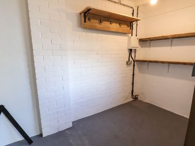 A room with white painted brick wall wooden shelves and hooks on the wall and a concrete floor at 18 Church Street in Llangollen