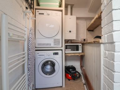 A laundry room with a stacked washer and dryer an ironing board a vacuum cleaner a microwave a boiler and shelves at 18 Church Street in Llangollen