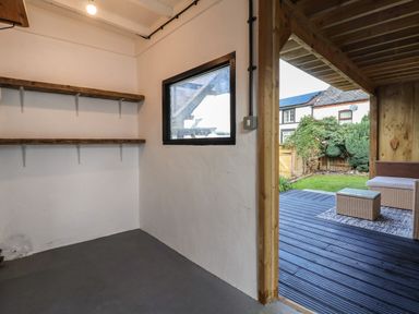 A room with two wooden shelves on the wall and a window looking outside to a deck with outdoor furniture and a garden at 18 Church Street in Llangollen