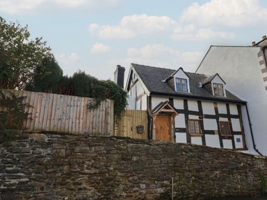 A black and white timber framed house behind a stone wall with a wooden fence at 18 Church Street in Llangollen