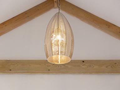 A hanging light fixture with a decorative metal shade and wooden beams on the ceiling at The Reading Room in Seworgan near Constantine
