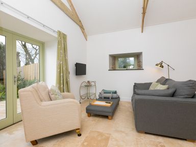 A living room with a beige armchair grey sofa ottoman and green curtains at The Reading Room in Seworgan near Constantine