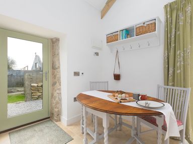 A dining area with a round wooden table and chairs near a green door and a wall shelf at The Reading Room in Seworgan near Constantine