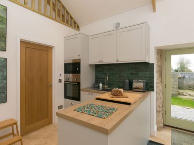 A kitchen with grey cabinets green tiled backsplash wooden door and a wooden countertop with bread at The Reading Room in Seworgan near Constantine