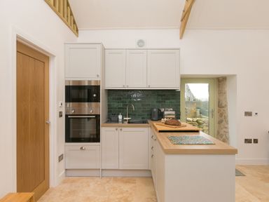 A kitchen with white cabinets green tiled backsplash wooden countertops and a door at The Reading Room in Seworgan near Constantine