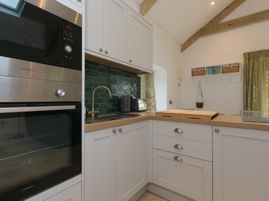 A kitchen with white cabinets a sink a microwave oven a toaster and green tiled backsplash at The Reading Room in Seworgan near Constantine