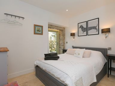 A bedroom with a double bed, bedside tables, wall lamps, and framed dog artwork at The Reading Room in Seworgan near Constantine