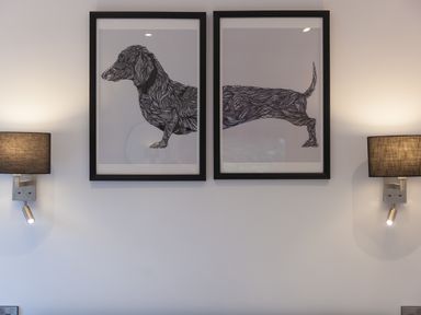 Two framed black and white abstract dog illustrations on a white wall with two wall-mounted lamps on each side at The Reading Room in Seworgan near Constantine