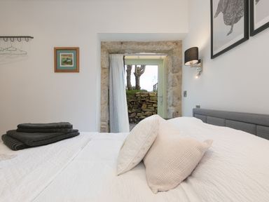 A bedroom with a bed pillows folded towels stone door frame and a small window at The Reading Room in Seworgan near Constantine