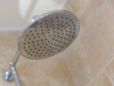 A close-up of a round showerhead attached to a wall with beige tiles at The Reading Room in Seworgan near Constantine