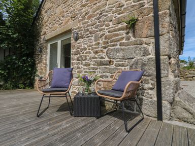Two wicker chairs with cushions and a small table with drinks on a wooden deck outside a stone building at The Reading Room in Seworgan near Constantine