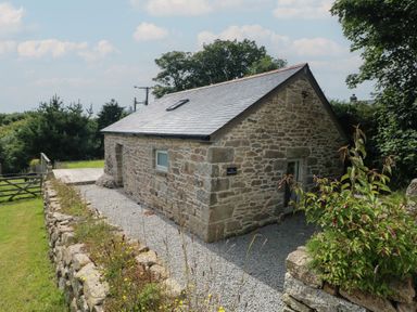 A stone building with a slate roof and gravel path surrounded by greenery at The Reading Room in Seworgan near Constantine