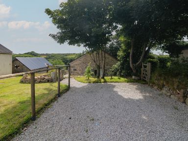 A gravel driveway with wooden fencing trees and stone buildings in a rural setting at The Reading Room in Seworgan near Constantine