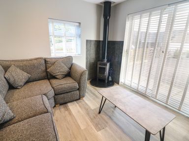 A living room with a gray corner sofa a wood burning stove and a table at White Stones in Goadsbarrow near Roose