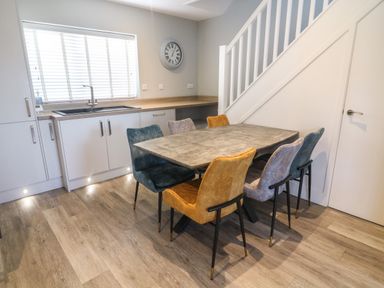 A kitchen with a dining table and six chairs near a staircase at White Stones in Goadsbarrow near Roose