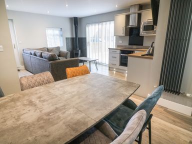 An open plan kitchen and living area with a dining table with chairs a grey sofa and kitchen units at White Stones in Goadsbarrow near Roose