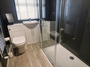 A bathroom with a toilet sink vanity unit shower enclosure and a window with blinds at White Stones in Goadsbarrow near Roose
