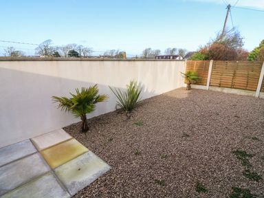 A gravel yard with small plants along a white wall and wooden fence at White Stones in Goadsbarrow near Roose