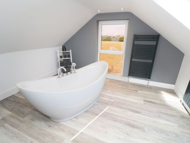 A bathroom with a freestanding bathtub, a window, a towel rack, and a small shelving unit with towels at White Stones in Goadsbarrow near Roose
