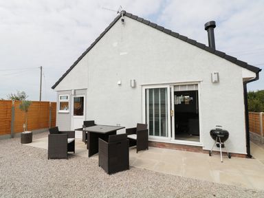 A backyard patio with black wicker chairs and table a charcoal grill a sliding glass door and a wooden fence at White Stones in Goadsbarrow near Roose