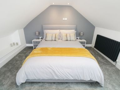 A bedroom with a bed with white bedding and a yellow throw with two bedside tables and lamps at White Stones Goadsbarrow near Roose