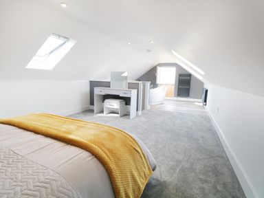 An attic bedroom with a bed with a yellow throw a vanity desk a bathtub and skylights at White Stones in Goadsbarrow near Roose