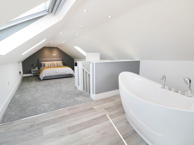 A bedroom with a bed and nightstand and a modern bathtub on wood flooring at White Stones in Goadsbarrow near Roose