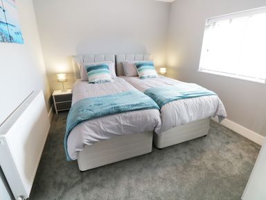 A bedroom with two single beds pushed together bedside tables lamps and a window at White Stones in Goadsbarrow near Roose