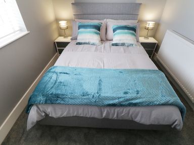 A bedroom with a bed with blue and white pillows and blanket two bedside tables and lamps at White Stones in Goadsbarrow near Roose