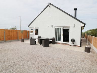 A backyard with a gravel ground a white house with a sliding door outdoor dining table with chairs and a barbecue at White Stones in Goadsbarrow near Roose